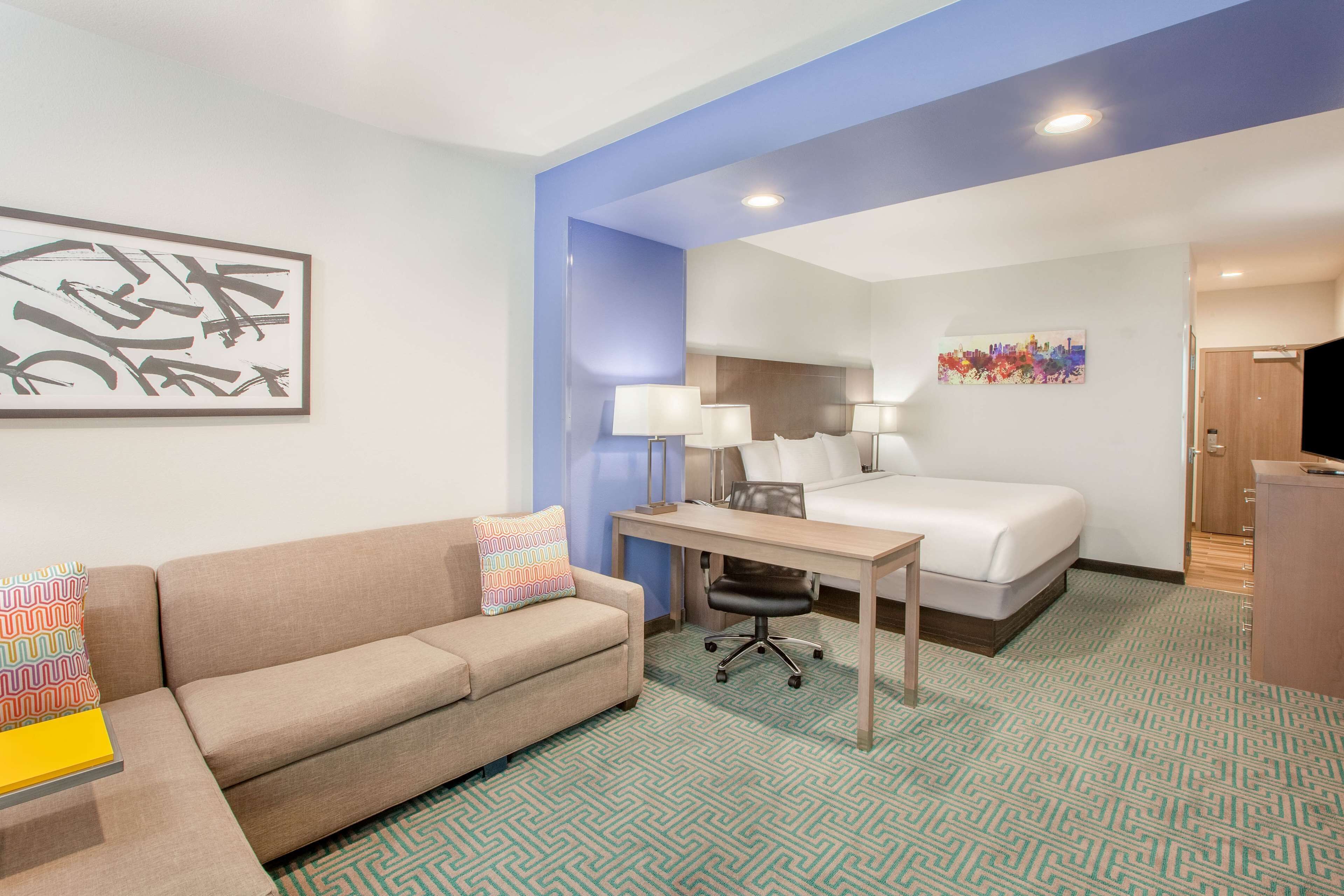 A hotel room with a bed, a desk, a chair, a sofa, and a painting on the wall.