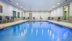 Una piscina con baldosas azules, rodeada de sillones de descanso y un ventanal de vidrio.