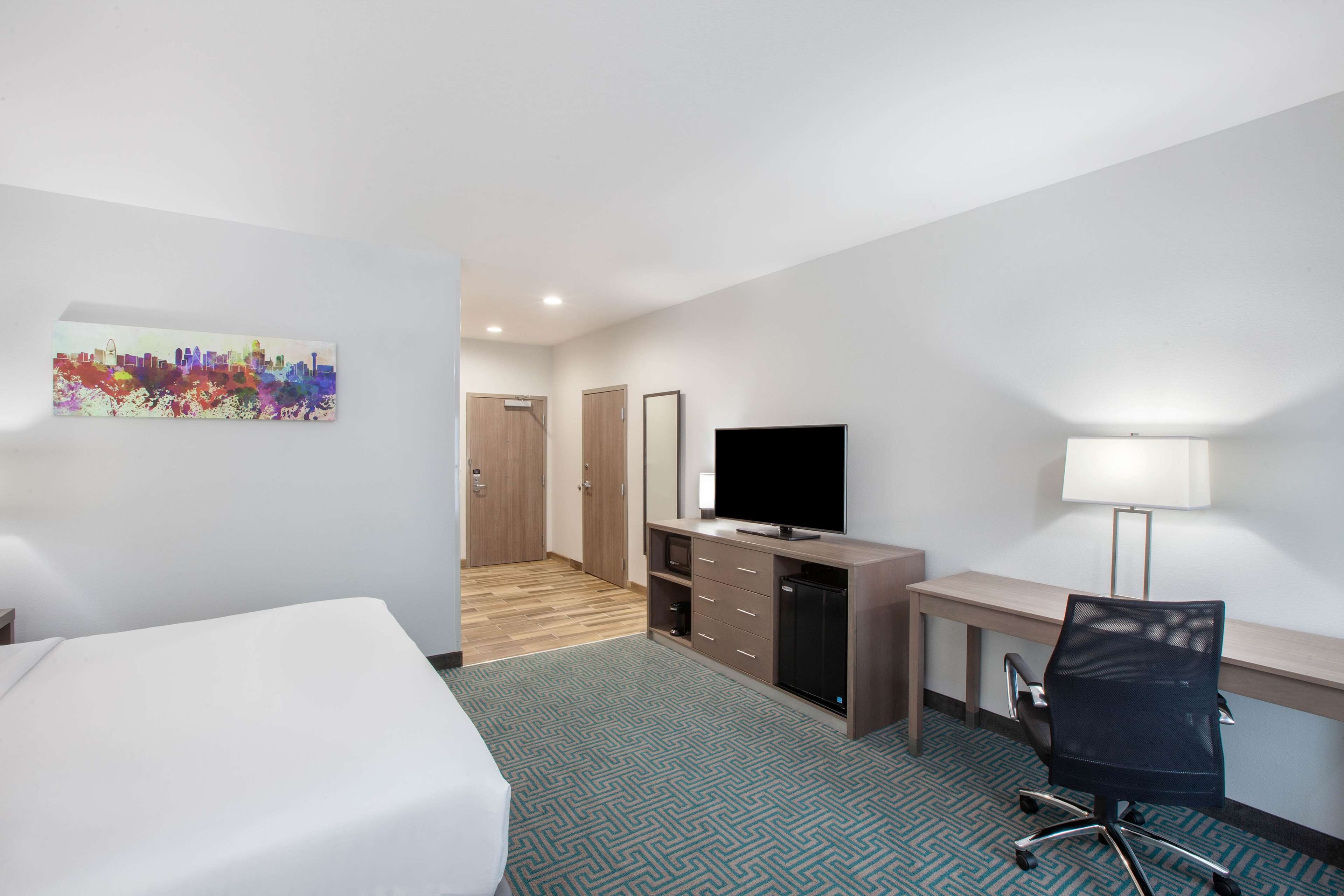 A hotel room with a bed, a desk with a computer, a TV, and a lamp.