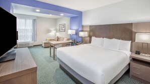 Habitación de hotel con una cama grande, un escritorio, una silla, un televisor y una ventana con cortinas.