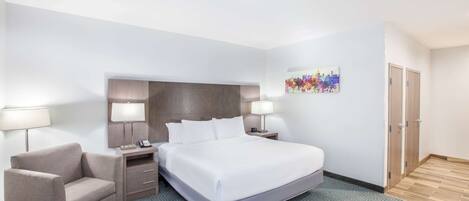 Une chambre d’hôtel avec un grand lit, deux tables de chevet, une chaise et une œuvre d’art accrochée au mur.