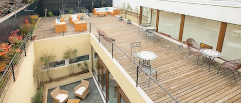 A multi-level outdoor deck with wooden flooring, wicker furniture, and glass railings.