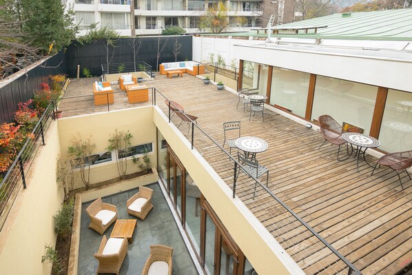 A multi-level outdoor deck with wooden flooring, wicker furniture, and glass railings.