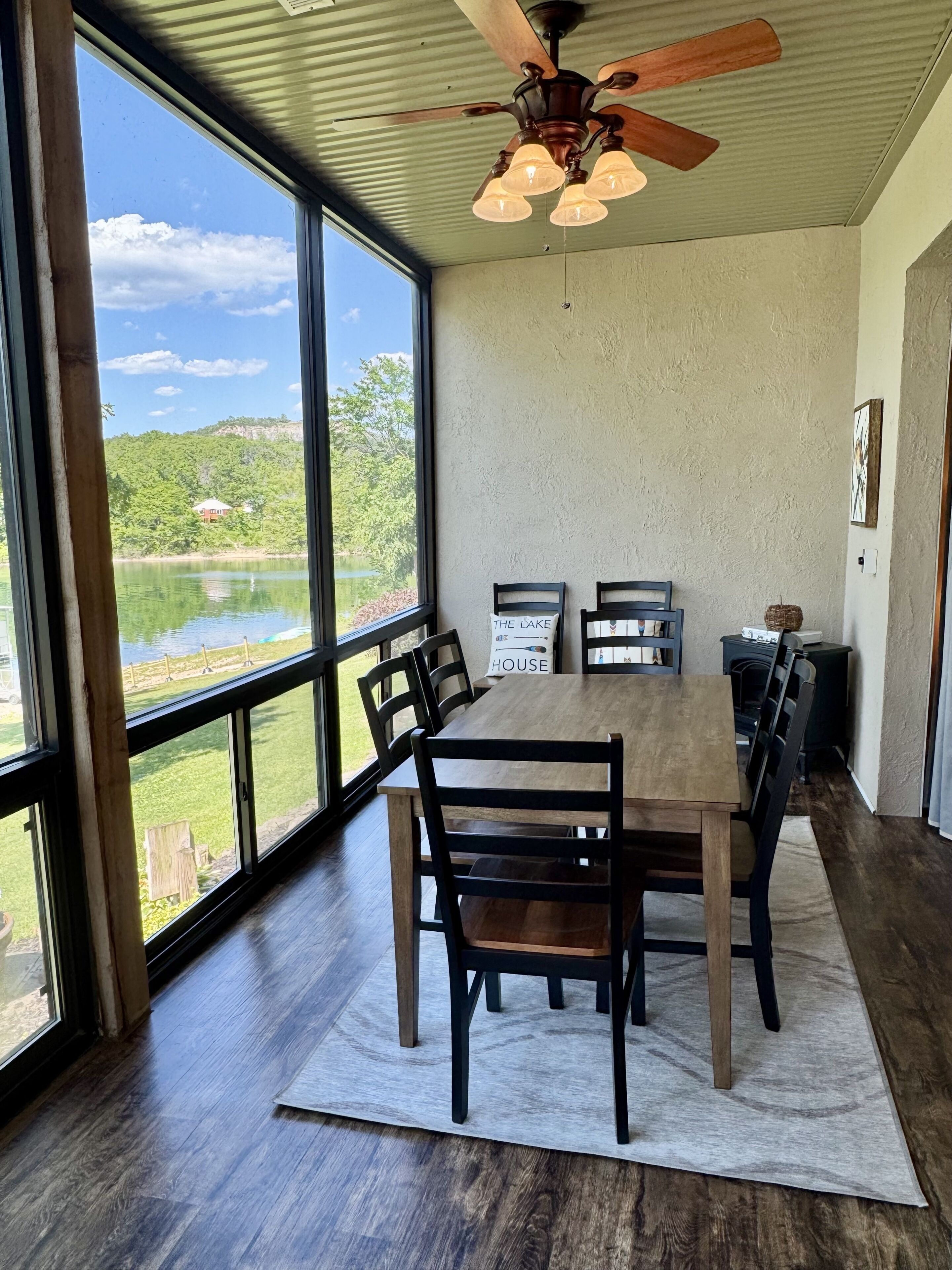 A dining area with a large table, chairs, a ceiling fan, and a view of a lake.
