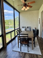Un comedor con una mesa grande, sillas, un ventilador de techo y vistas a un lago.