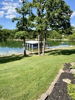 Vista del lago con un pabellón, árboles y un edificio al fondo.