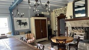 A dining area with a long wooden table, several chairs, a chandelier, a stone fireplace, and a large mirror.