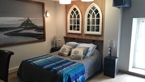 A bedroom with a bed, a nightstand, a lamp, a chair, a painting, and a window.