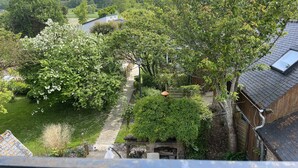 A residential area with a pathway leading to a house with a visible chimney and a garden with flowering bushes.