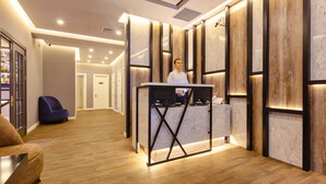 A reception area with a marble reception desk, a blue chair, and a wooden floor. - Aksent Hotel (Baku)