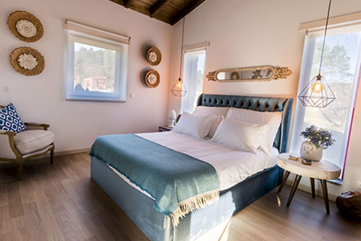 A bedroom with a large bed, a chair, a small table with a plant, and decorative wall items.