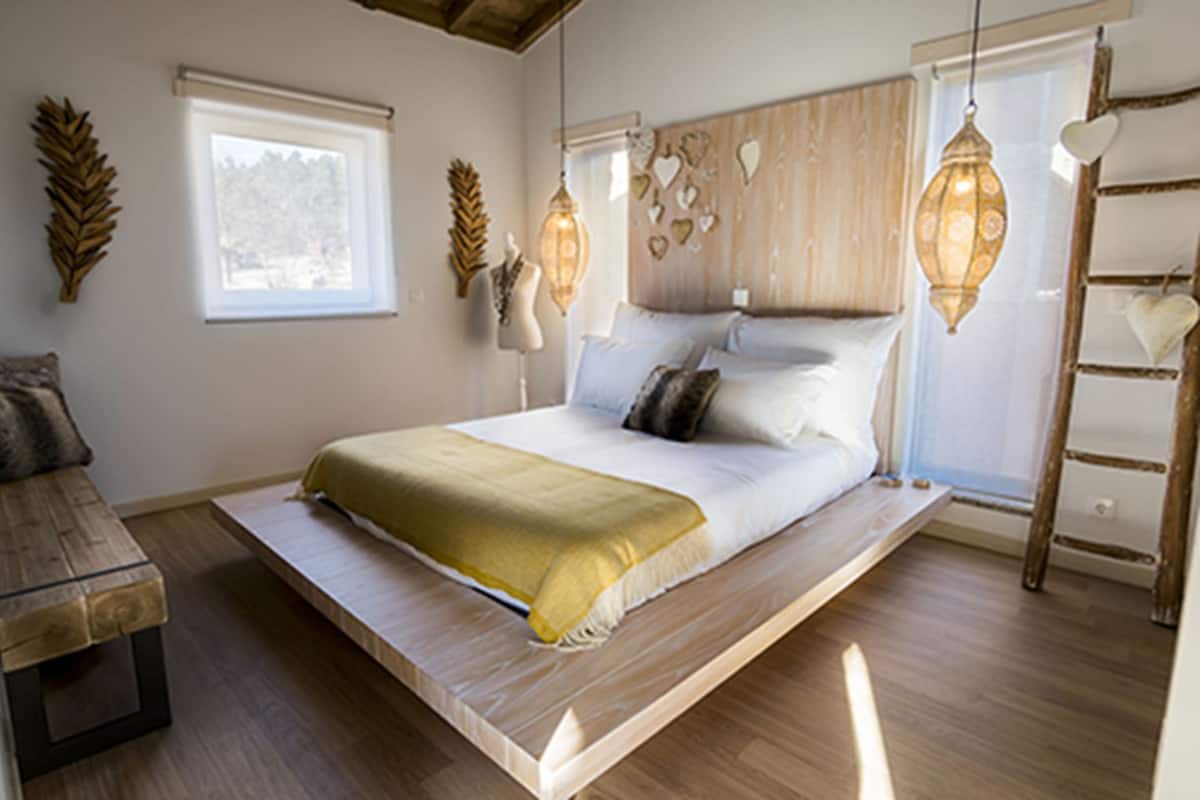 A bedroom with a bed, wooden floor, a bench, and a ladder.