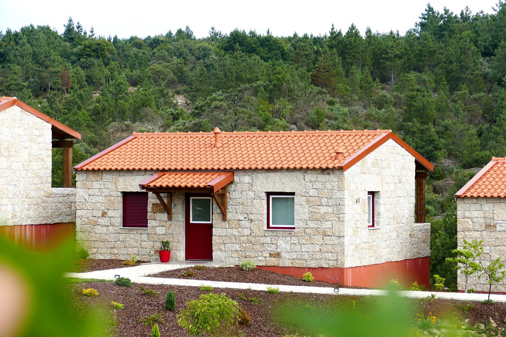 Una casa de piedra con techo de tejas rojas, una puerta roja y una ventana pequeña.