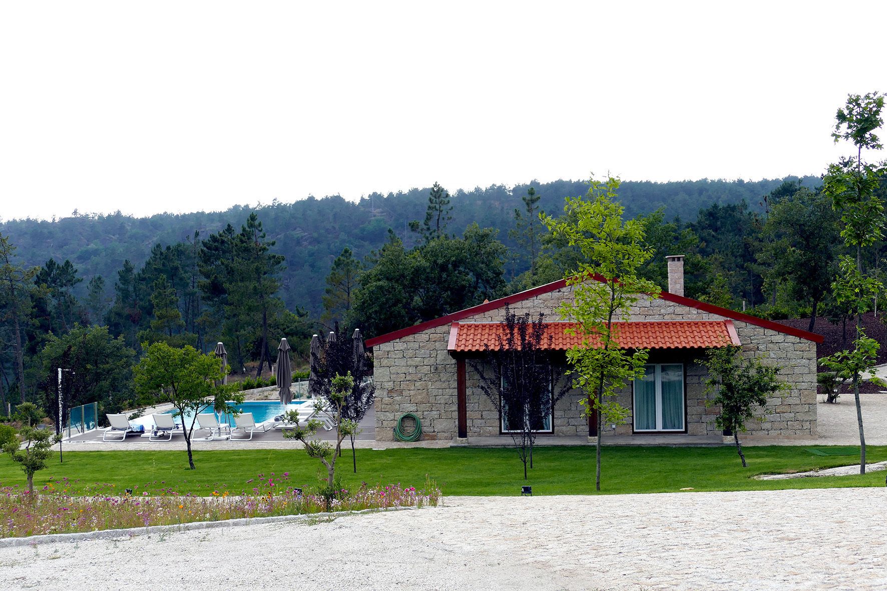 A stone building with a red-tiled roof, a swimming pool, and a grassy area with trees.