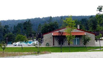 A stone building with a red-tiled roof, a swimming pool, and a grassy area with trees.