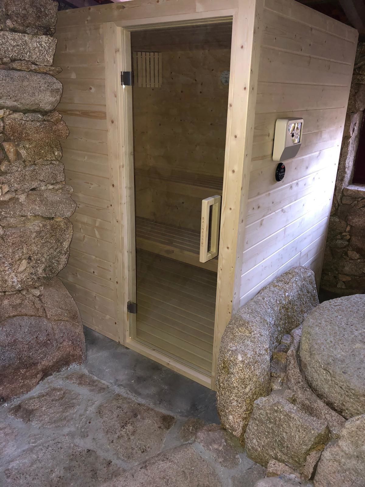 Una sauna in legno con porta scorrevole, pareti in pietra e pannello di controllo sulla destra.