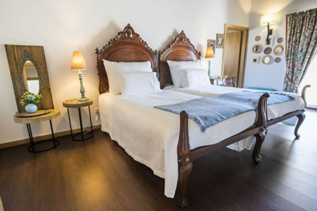 A double bed with a wooden headboard, two bedside tables with lamps, a mirror, and a wall with decorative plates.