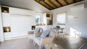 A modern living room with a sofa, a dining table with chairs, a kitchen area, and a large window allowing natural light. - Moinho da Lapa (Sernancelhe)