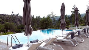 A poolside area with lounge chairs and umbrellas, surrounded by a natural landscape. - Moinho da Lapa (Sernancelhe)
