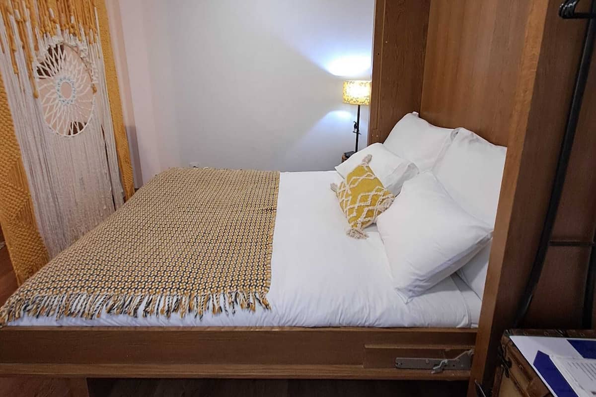 A single bed with a wooden frame, white bedding, and a patterned throw.