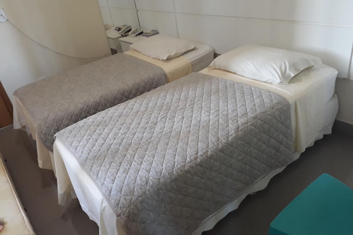 Two single beds with white linens and a small bedside table with a telephone.