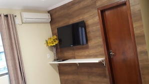 A bedroom with a bed, a mounted TV, a wooden wall panel, a door, and a window with curtains. - Hotel Loureiro (Rio Branco)