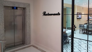 An elevator with a digital display indicating the floor level, a wall-mounted sign reading "Restaurant," and a glimpse of a dining area with tables and chairs. - Hotel Loureiro (Rio Branco)
