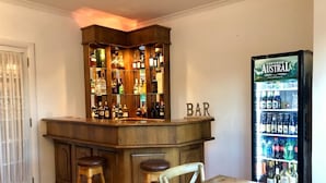 En bar med træbordplade, barstole og et køleskab fyldt med drikkevarer.