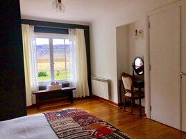 A bedroom with a large window, a bed, a bench with towels, a chair, and a radiator.