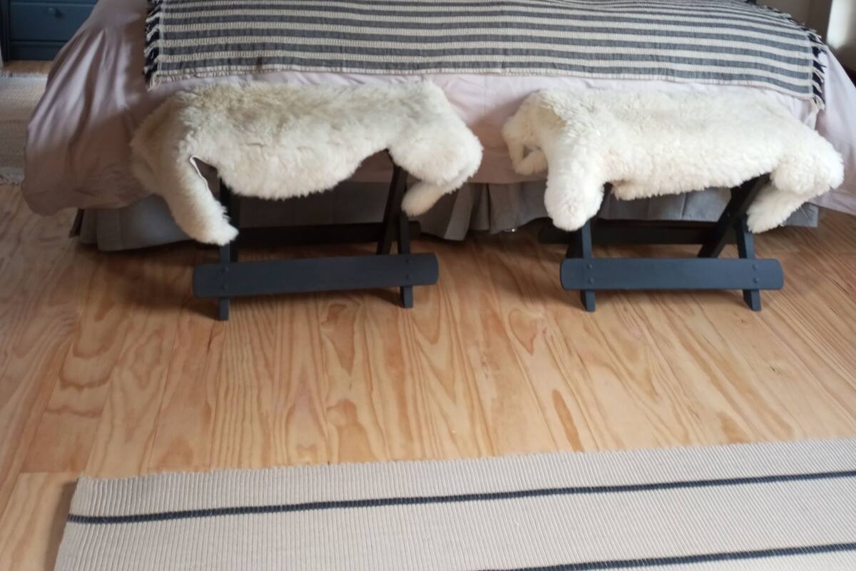 Une chambre à coucher avec un lit, deux tables de chevet, une lampe sur chacune, un plancher en bois et une tête de lit ornée d’un motif tissé.
