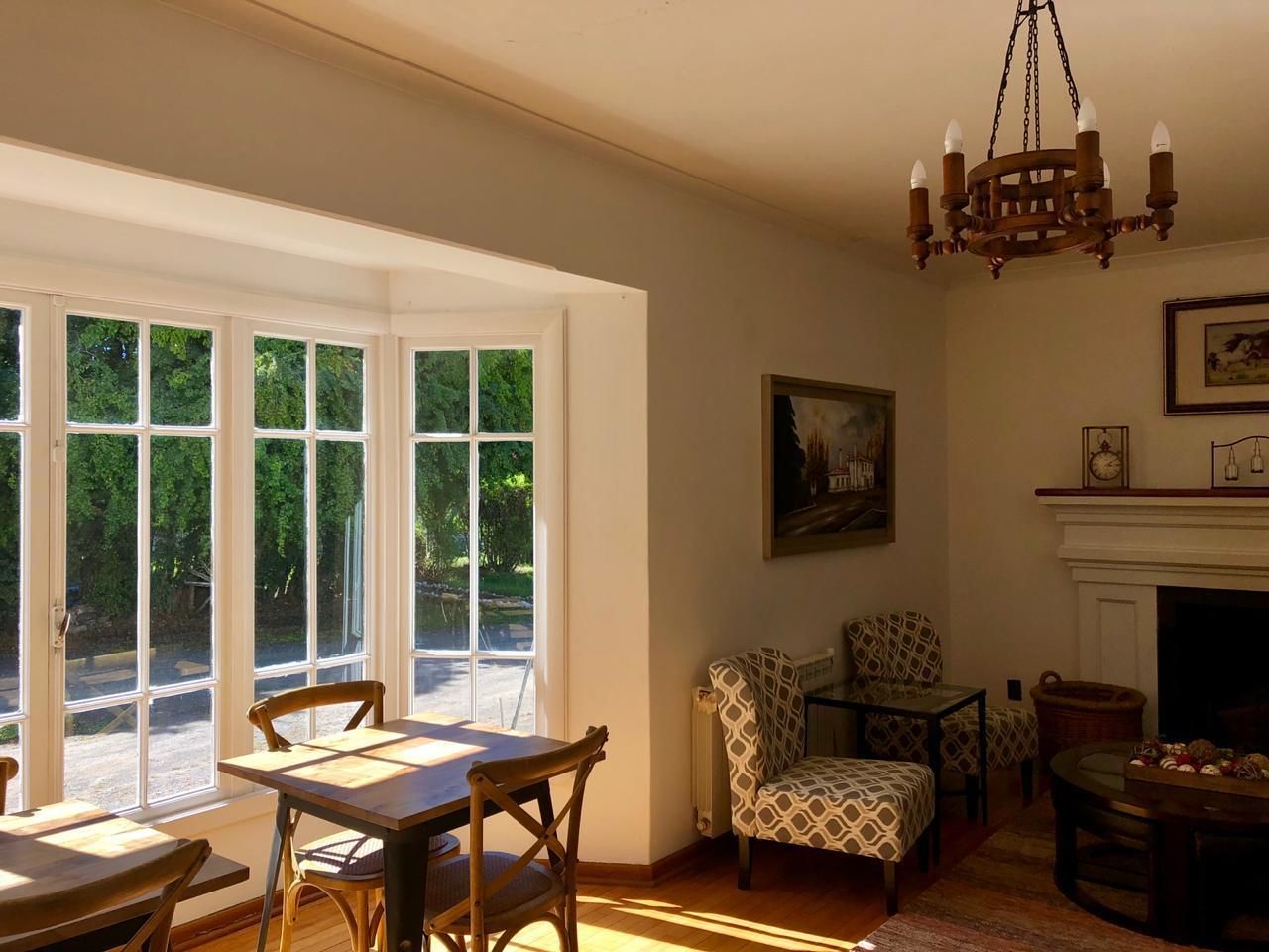 Une pièce comprenant une table à manger, des chaises, un fauteuil à motifs, une cheminée et un lustre.