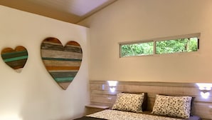 A bedroom with a bed, two heart-shaped wall decorations, a window, and a wooden headboard. - El Pasito (Tempate)