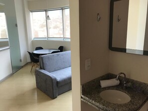 A small, modern room with a grey sofa, a round table, and a large window. - Locking Funcionarios (Belo Horizonte)