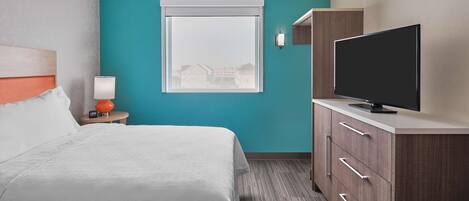 A hotel room with a bed, a TV on a cabinet, a window with a view, and a nightstand with a lamp.
