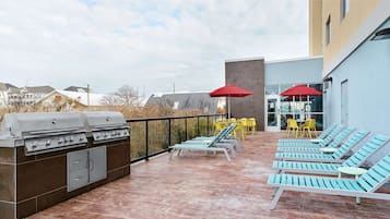 Une terrasse extérieure avec un barbecue, des fauteuils de jardin jaunes et bleus, et des parasols rouges.