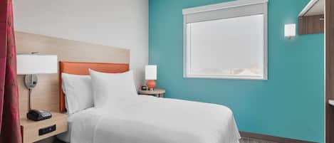 Une chambre d’hôtel avec un lit, une table de chevet avec un téléphone, une lampe et une fenêtre avec des stores.