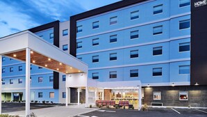 Un hotel de varios pisos con diseño moderno, que cuenta con una entrada cubierta y un área de restaurante visible con mesas al aire libre.