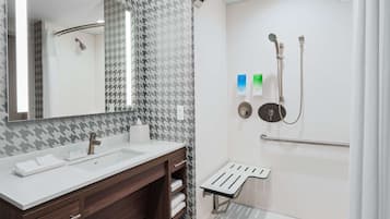 A modern bathroom with a dual sink vanity, a mirror, a shower with a handheld showerhead, and a grab bar.