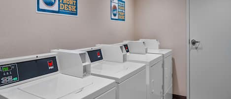A row of white front-loading washing machines in a laundry room with a door on the right.