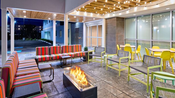 Un área de estar al aire libre con sofás y sillones de colores a rayas, una chimenea y vistas del edificio al fondo.