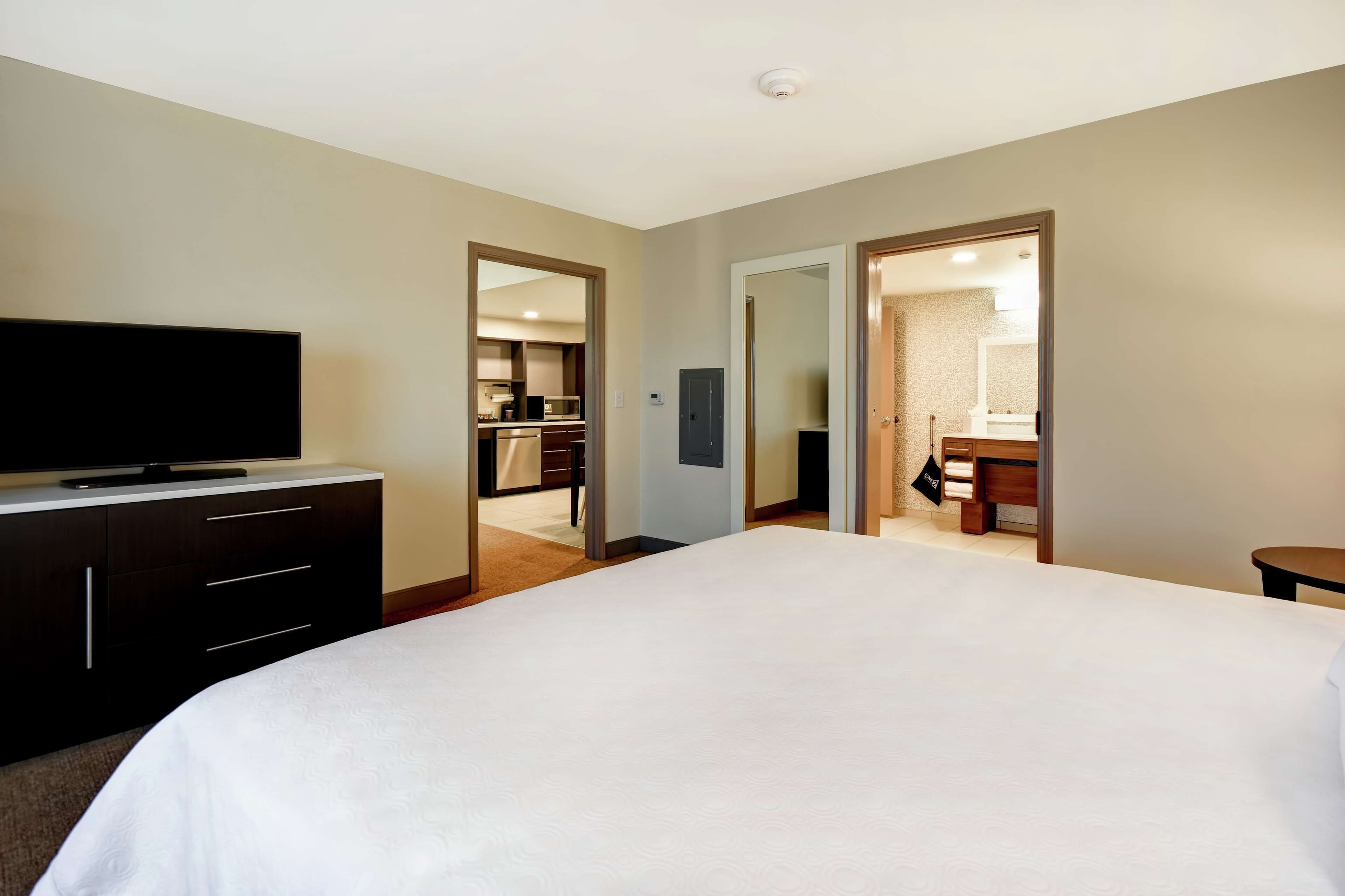 Habitación de hotel con una cama grande, un televisor en una cómoda, un espejo y vistas al baño y la cocina a través de una puerta abierta.