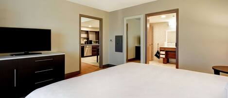 Habitación de hotel con una cama grande, un televisor en una cómoda, un espejo y vistas al baño y la cocina a través de una puerta abierta.