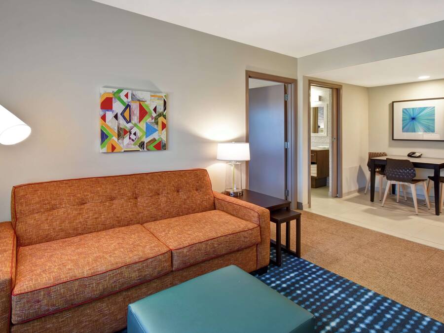 Une chambre d’hôtel avec un canapé, une petite table avec une lampe, un coin repas avec des chaises et un tableau au mur.
