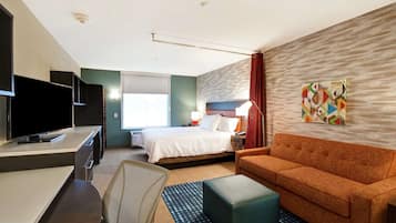 Una habitación de hotel con una cama, un escritorio con televisor, un sofá y un cuadro geométrico en la pared.
