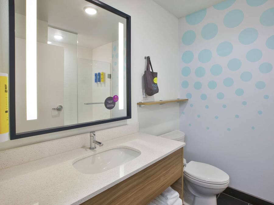 A bathroom with a white sink, mirror, and toilet. There is a shelf above the toilet and a wall with blue polka dots.