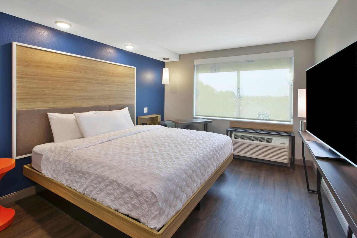 A modern hotel room with a wooden bed frame, a large window with a view, a flat-screen TV, and a heater.
