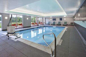 An indoor swimming pool with clear glass walls, red and green lounge chairs, and a no diving sign.