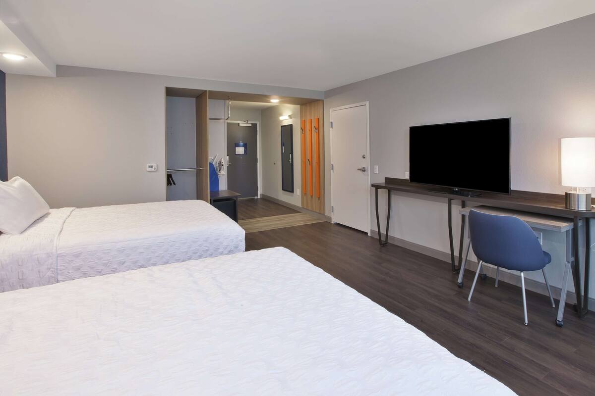 A hotel room with two beds, a desk with a TV, and a chair.