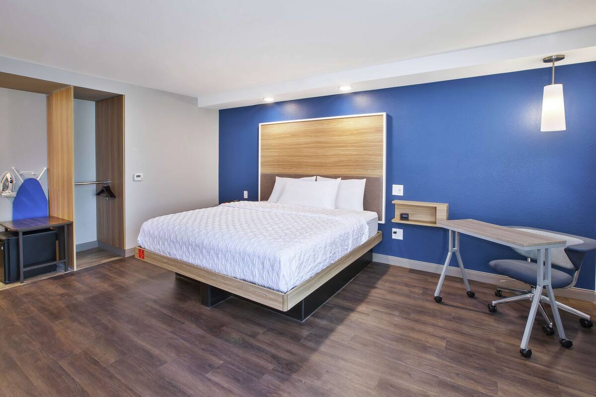 A modern hotel room with a wooden bed, a desk, and a chair.