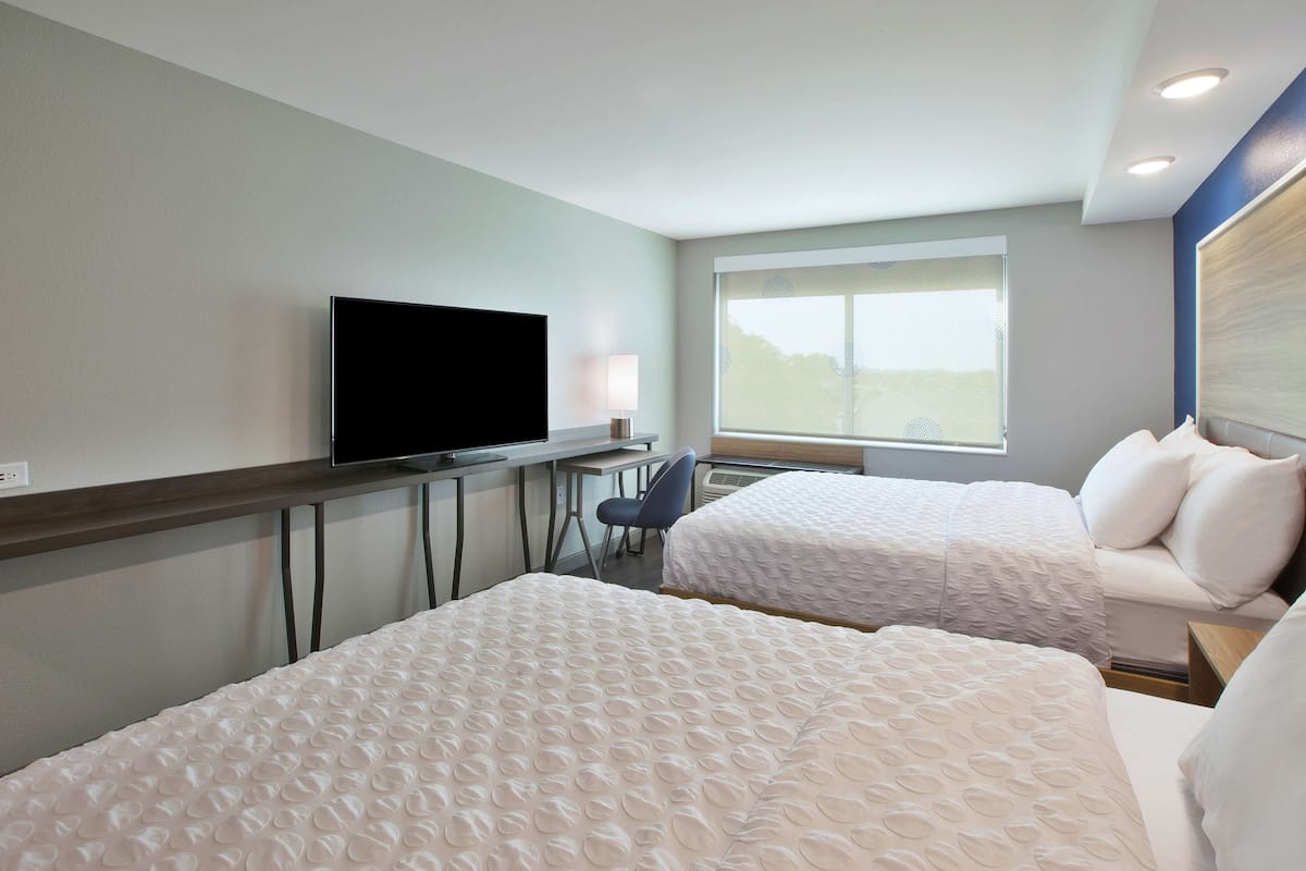 A hotel room with two beds, a desk, a chair, a TV, and a window with a view.
